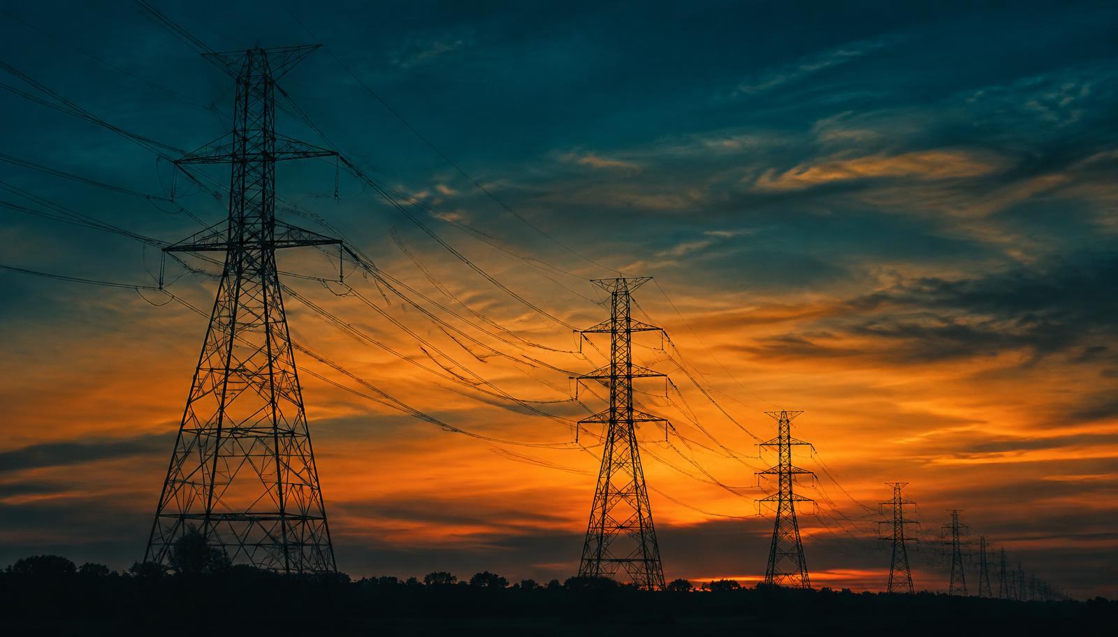 High-voltage transmission towers silhouetted against an amber dusk sky
